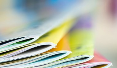Close-up of colorful magazines stacked in a neat pile with blurred background.