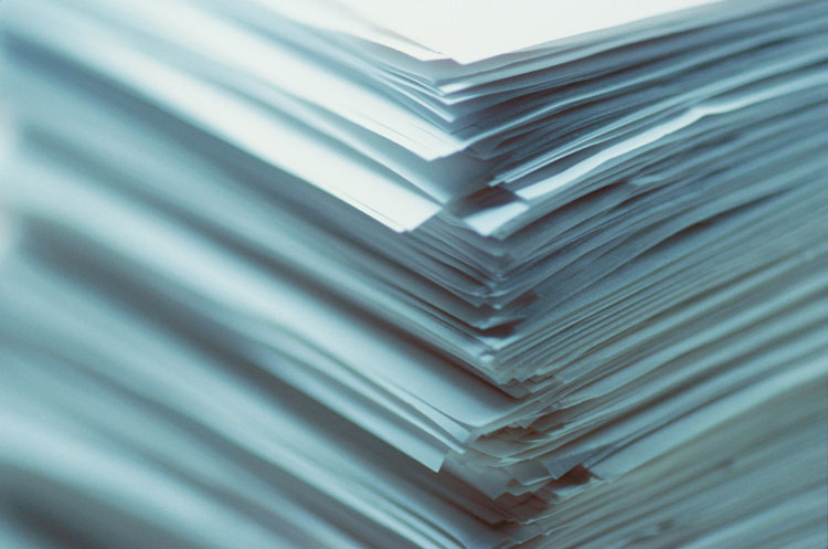 A close-up of a large, messy stack of white papers with uneven, visible edges.