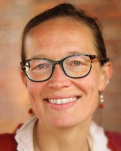 A smiling woman with glasses, earrings, and a red sweater over a white collared shirt.