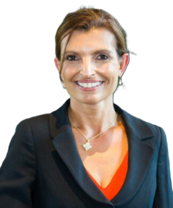 A woman with light brown hair smiles, wearing a blazer, orange top, and necklace against a white background.